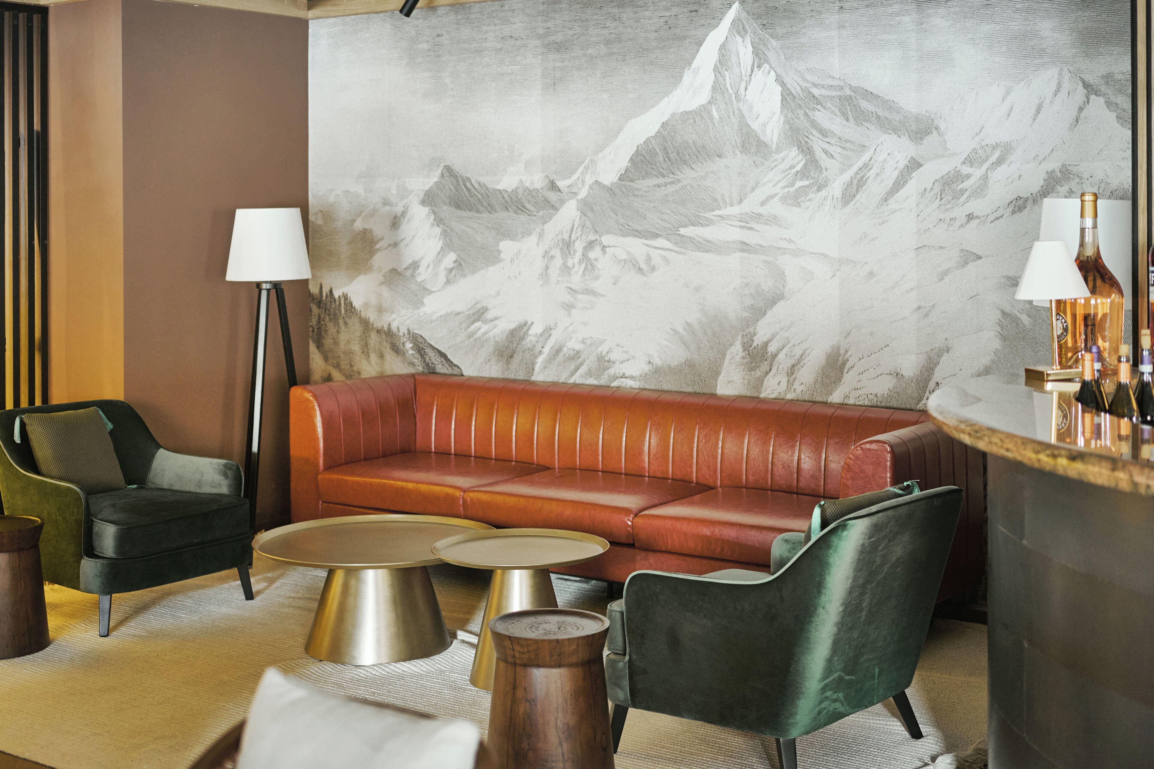 Un salon moderne comprenant un canapé en cuir, deux fauteuils, une table basse et un coin bar agrémenté d’un grand tableau représentant des montagnes.