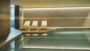 Un área de spa con piscina, tres tumbonas de madera y una pared con textura.
