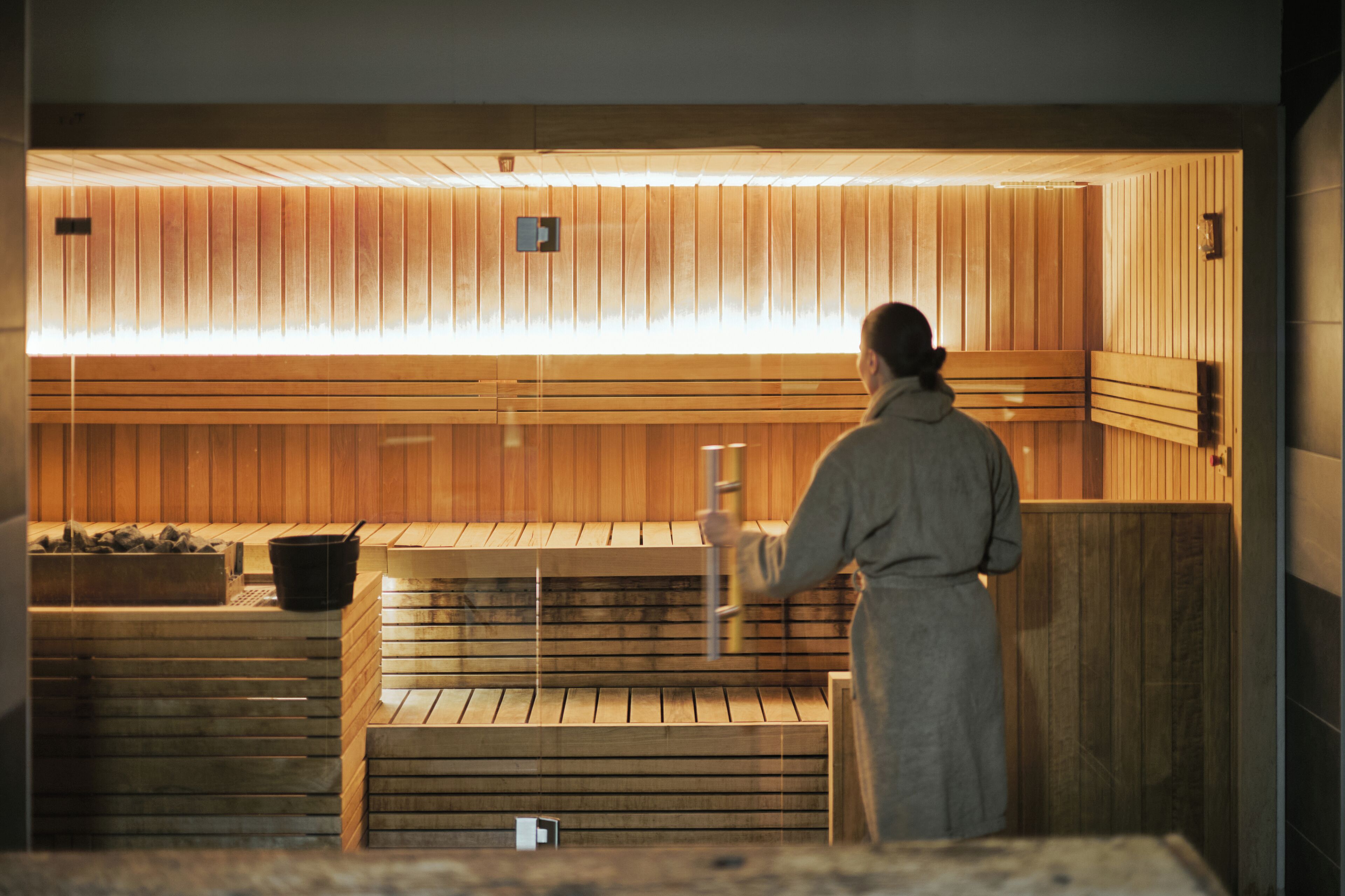 Una sauna con panche in legno e una persona che vi sta davanti.