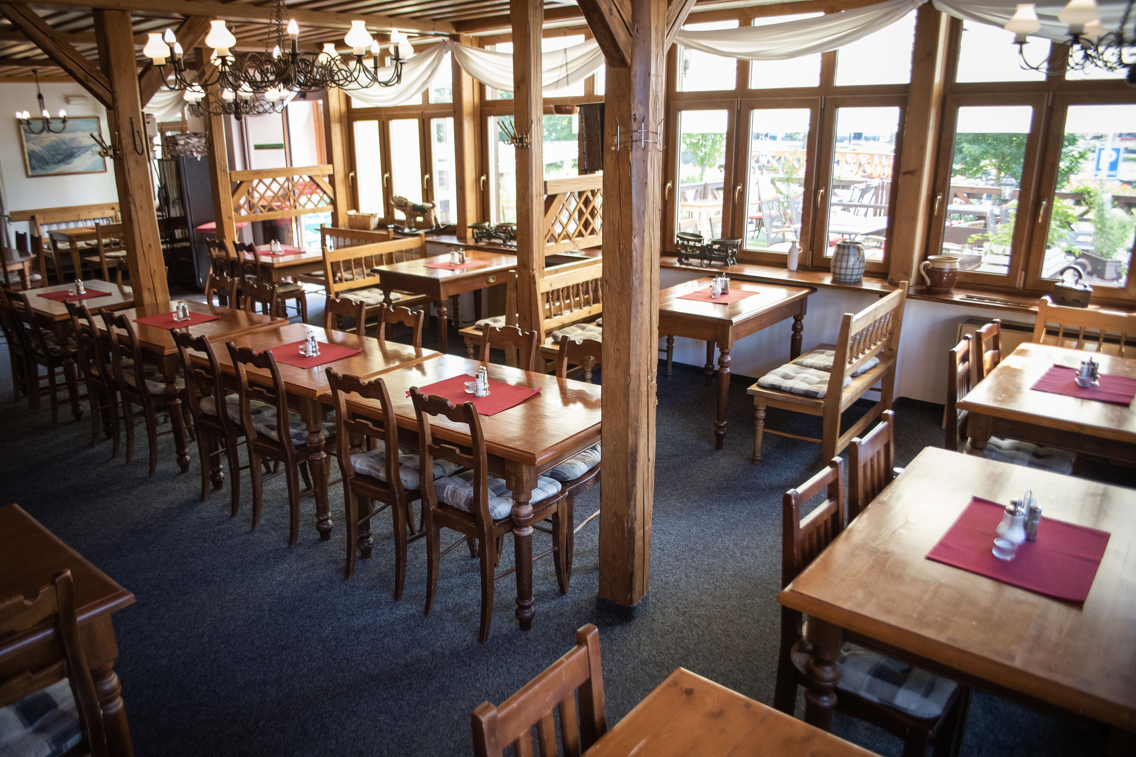A restaurant with wooden tables and chairs, large windows, and a chandelier.