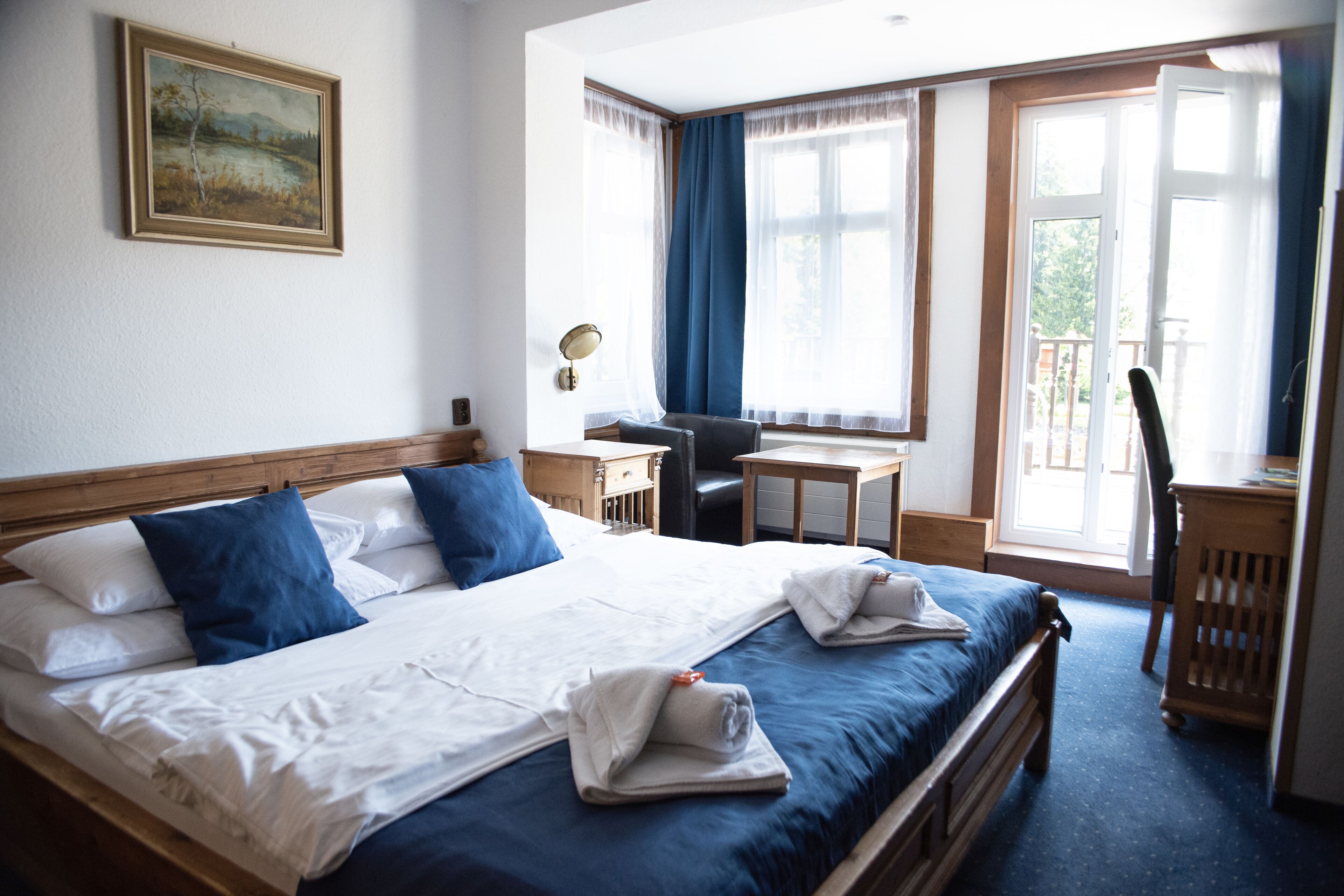 Habitación de hotel con una cama grande, un escritorio, una silla y vistas al exterior a través de las ventanas.
