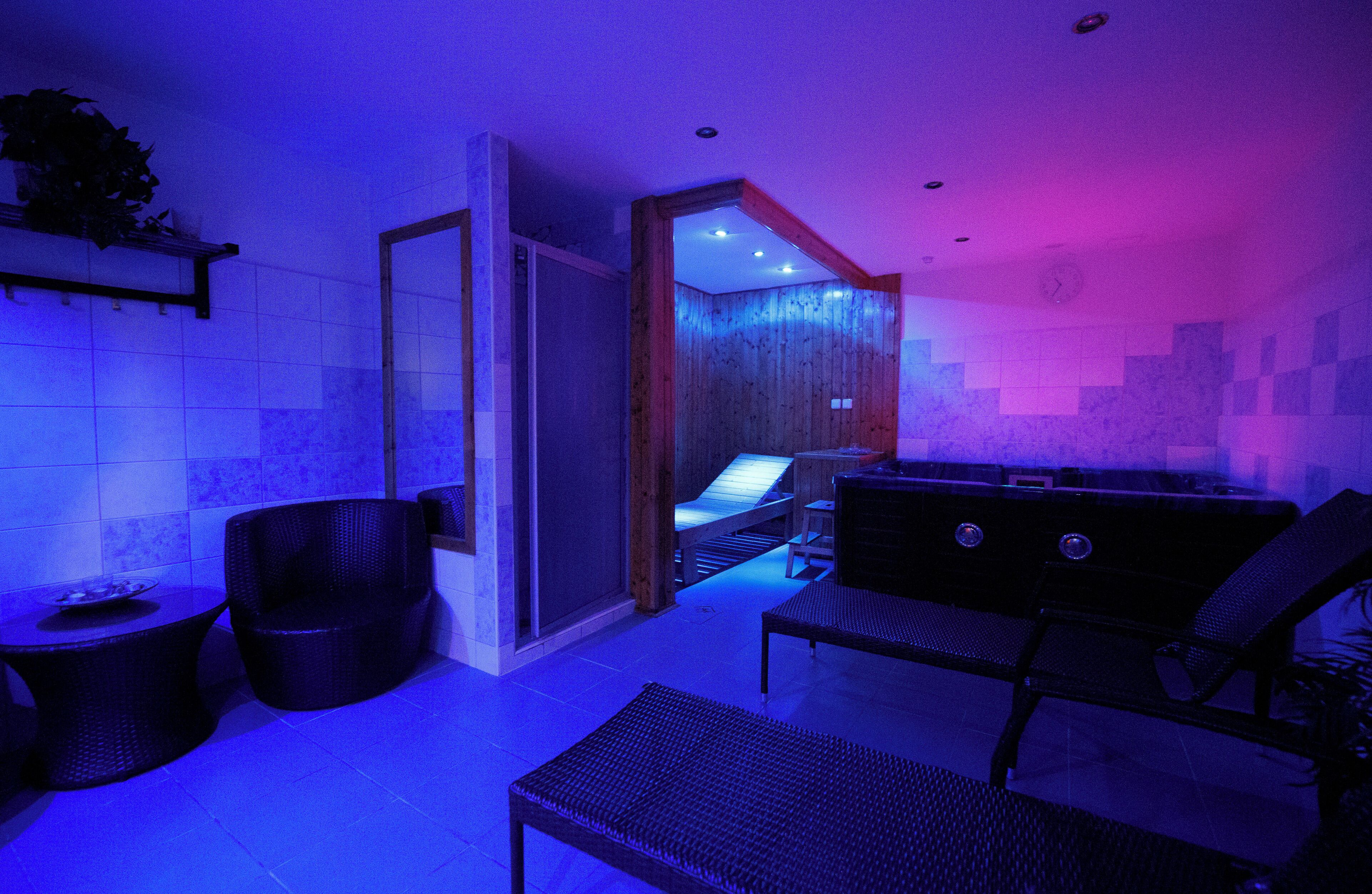 A modern spa room with a glass-enclosed hot tub, a seating area with lounge chairs, and a small table with a bowl.