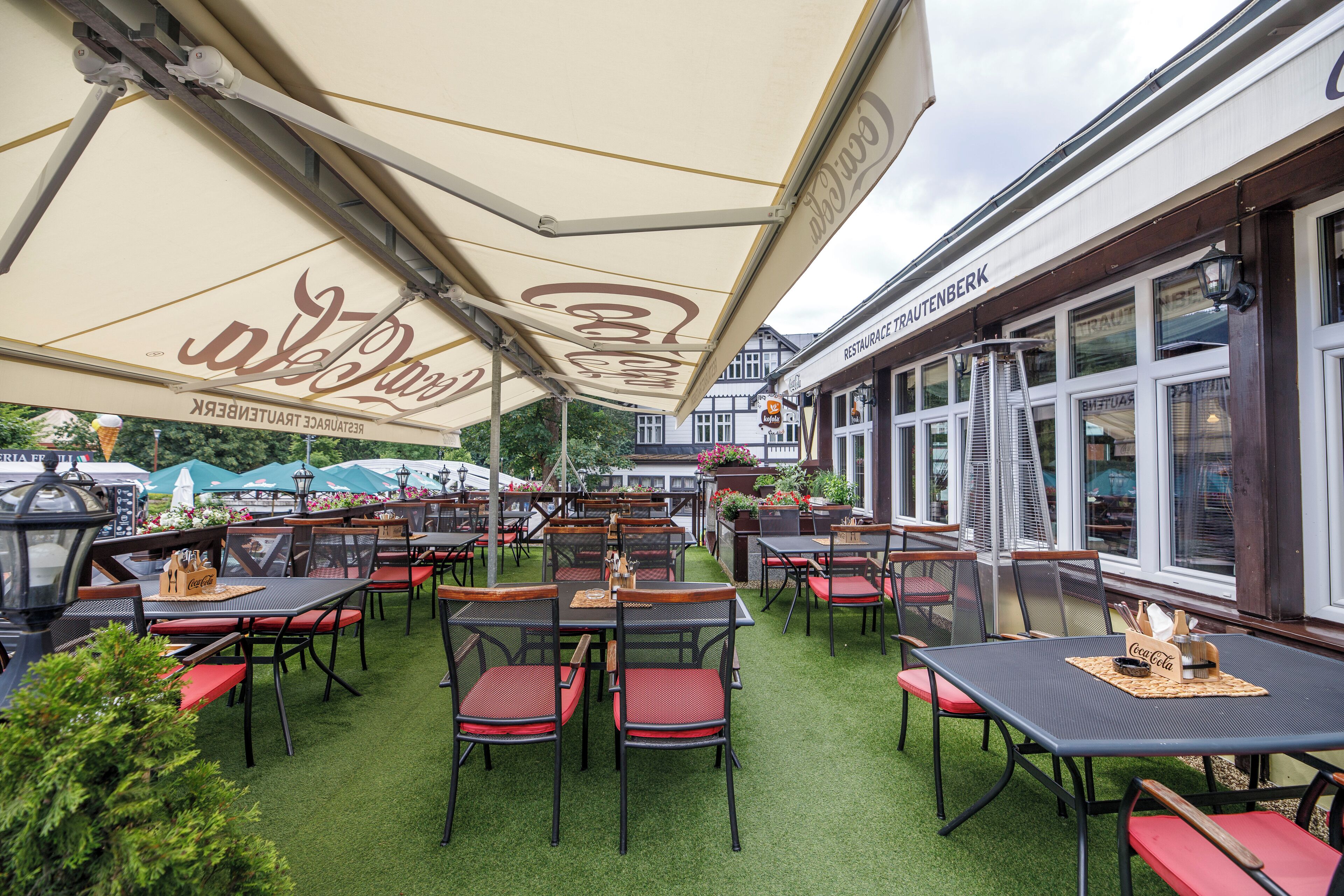 An outdoor dining area with tables and chairs, umbrellas, and a building with a sign.