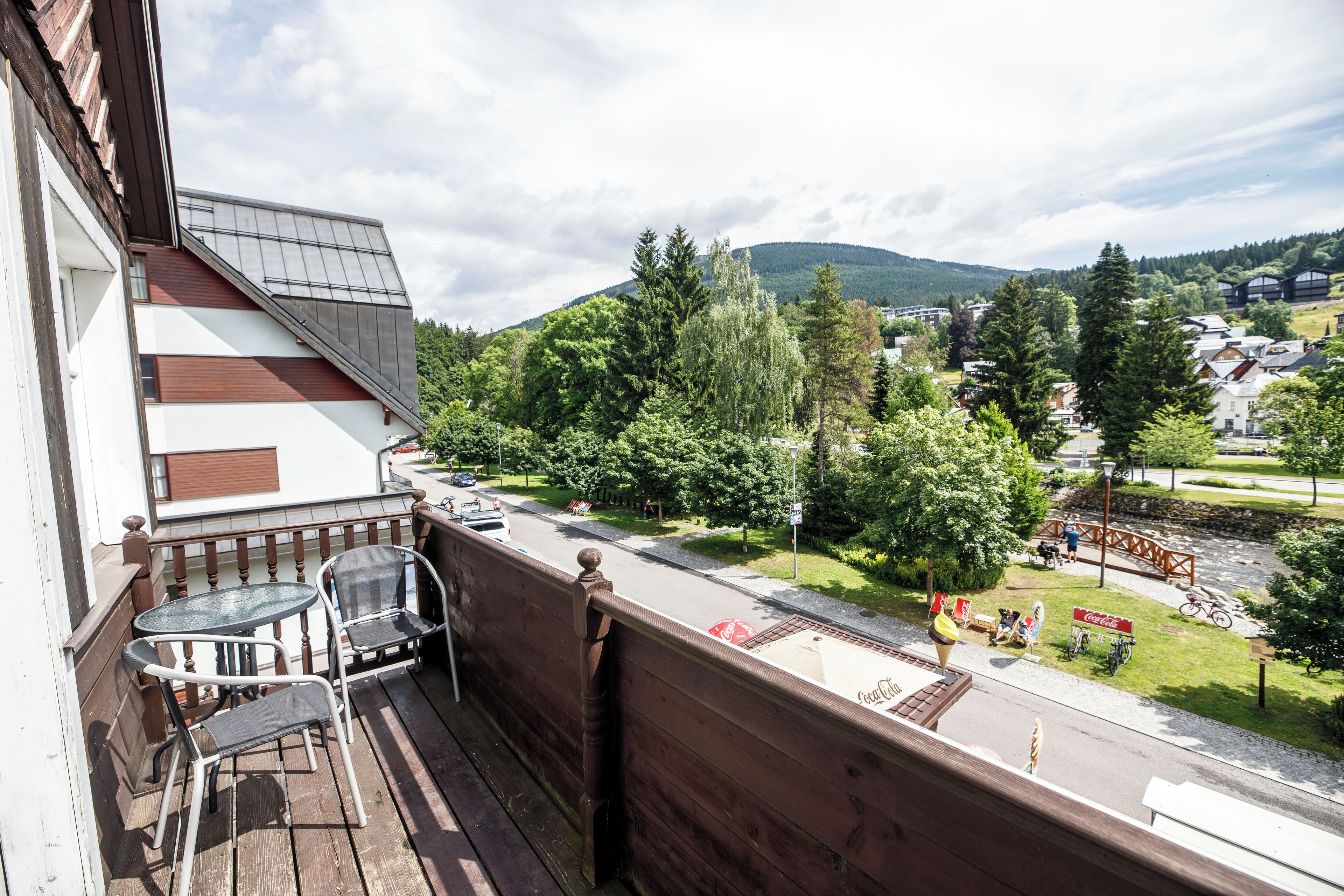 A balcony with a wooden railing, two chairs, and a view of a town with houses, trees, and a mountain in the background.