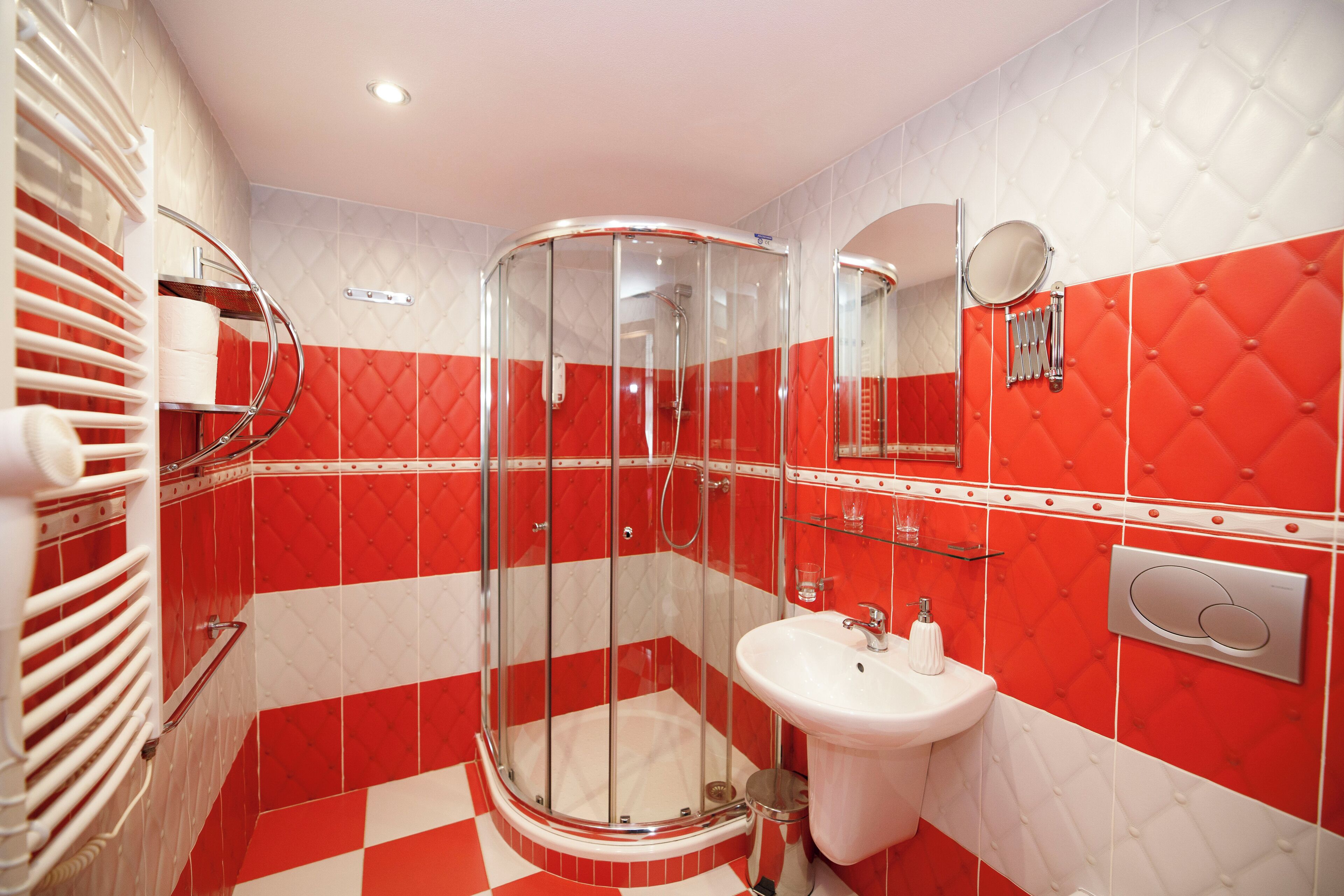 Un baño con ducha envuelta en vidrio, un lavamanos blanco y paredes con diseño rojo y blanco.