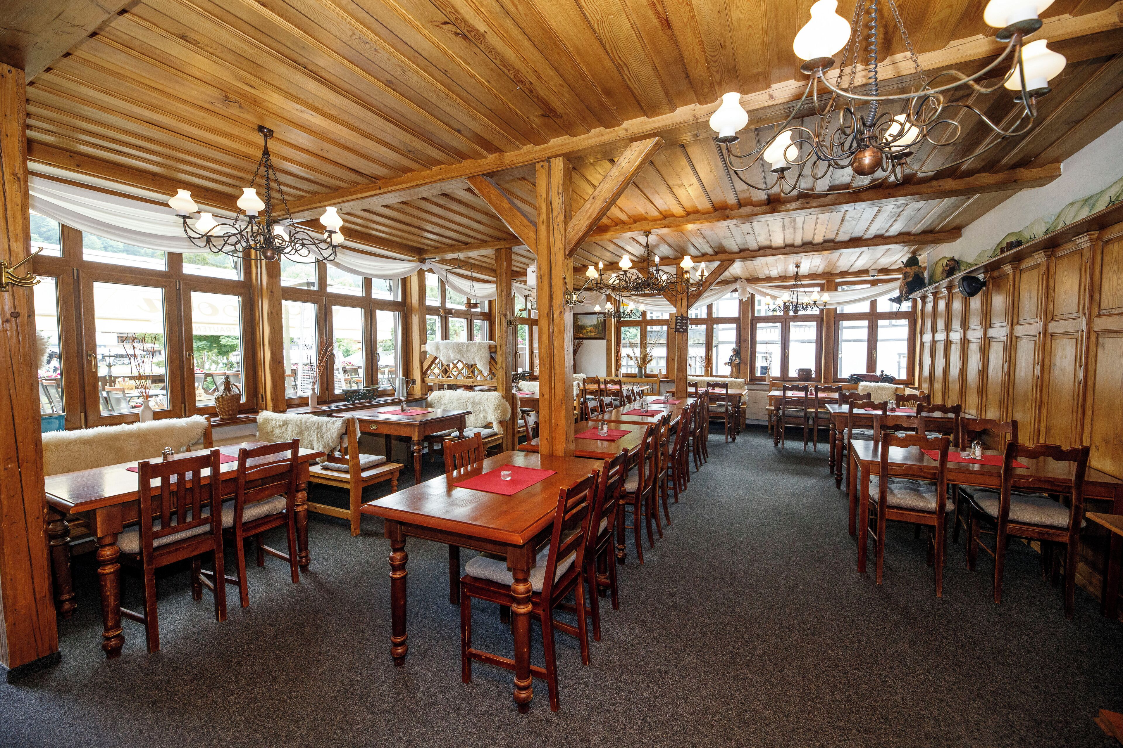 A spacious dining area with wooden tables and chairs, large windows, and a high wooden ceiling with chandeliers.