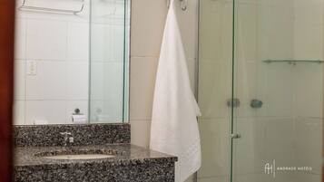 A bathroom with a granite countertop sink, a glass shower enclosure, and a white towel hanging on a metal rack.