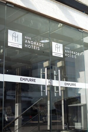Entrada de hotel com portas de vidro identificadas com "REDE ANDRADE HOTÉIS" e "EMPURRE".