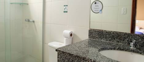 A bathroom with a glass shower enclosure, a white toilet, and a granite countertop sink.
