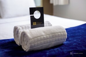 Toalha branca dobrada com um cartão de hotel sobre um cobreleito azul.