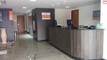 Zona de recepción con un mostrador de madera, una computadora y un cartel que indica las tarifas de las habitaciones.