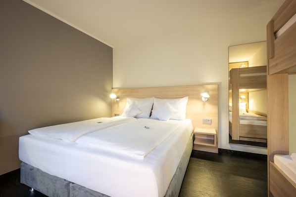 A neatly made bed with white linens, a wooden headboard, and bedside lamps. - Serways Hotel Bruchsal West (Forst)