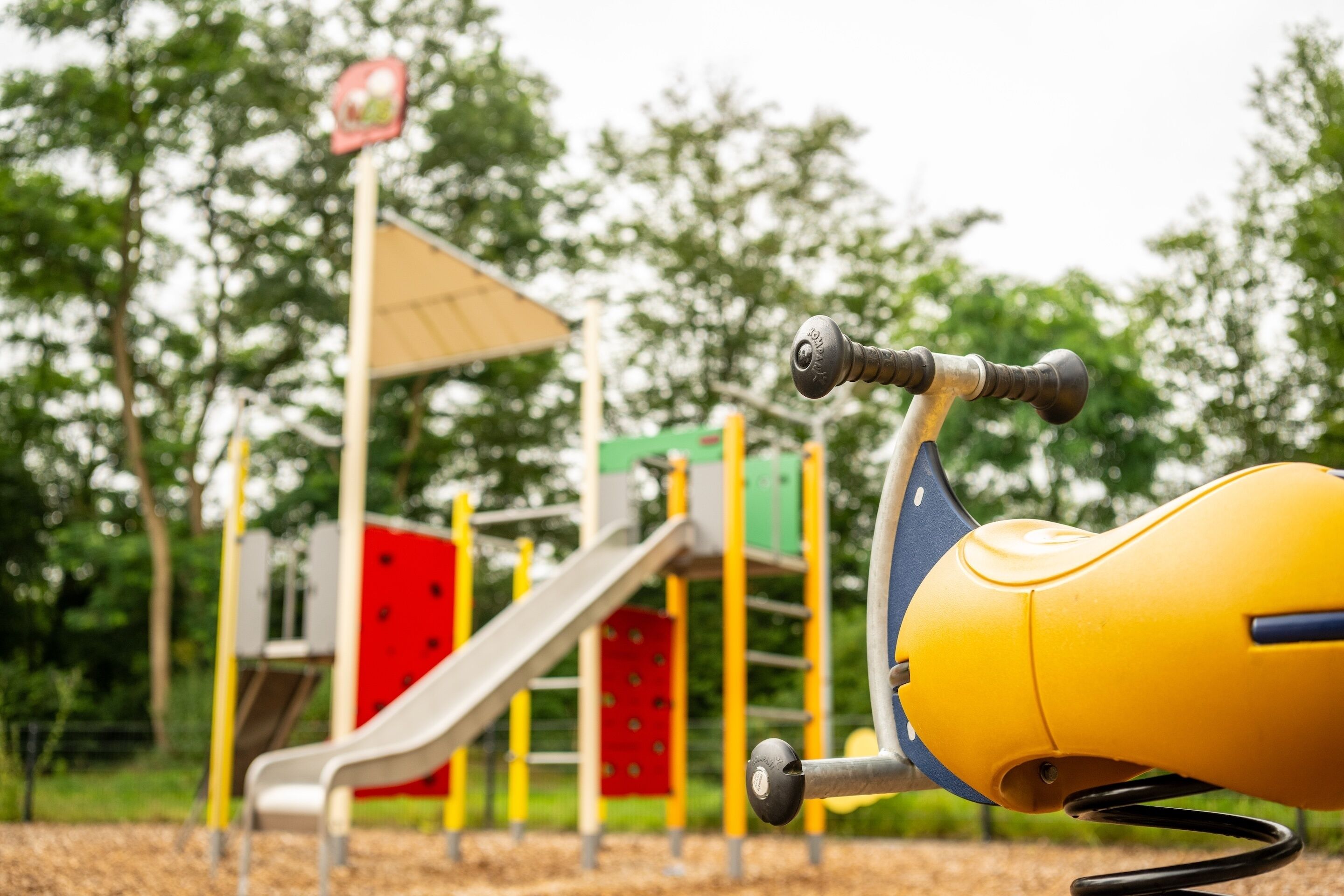 A playground with a yellow swing set and a slide.