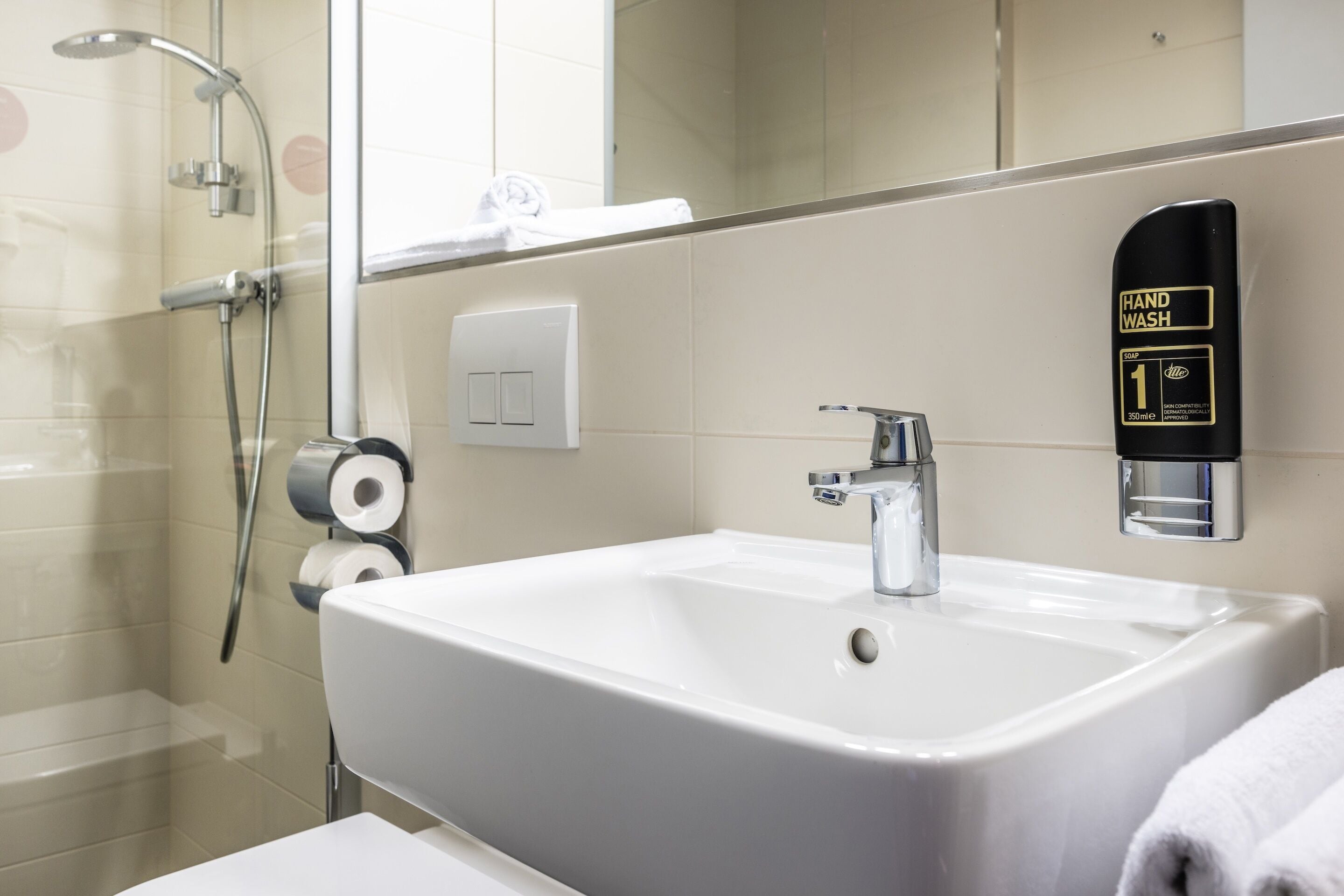 Un baño con un lavamanos blanco, dispensador de jabón y ducha.