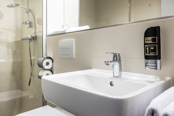 Un baño con un lavamanos blanco, dispensador de jabón y ducha.
