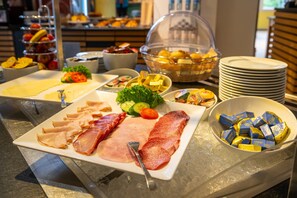 Un bufé con diversas opciones de comida, incluyendo carnes, quesos y frutas.