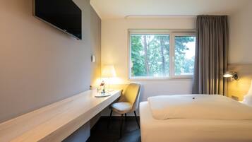 Une chambre d’hôtel équipée d’un lit, d’un bureau, d’une chaise, d’un téléviseur fixé au mur et d’une fenêtre avec des rideaux.
