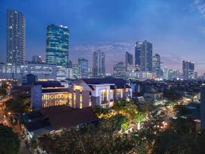 A cityscape at dusk with modern high-rise buildings, a prominent curved skyscraper, and residential areas with well-lit houses. - Rasuna Mansion (Jakarta)