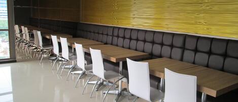 A conference room with long tables and white chairs, a wooden panel wall, and a black cushioned bench.