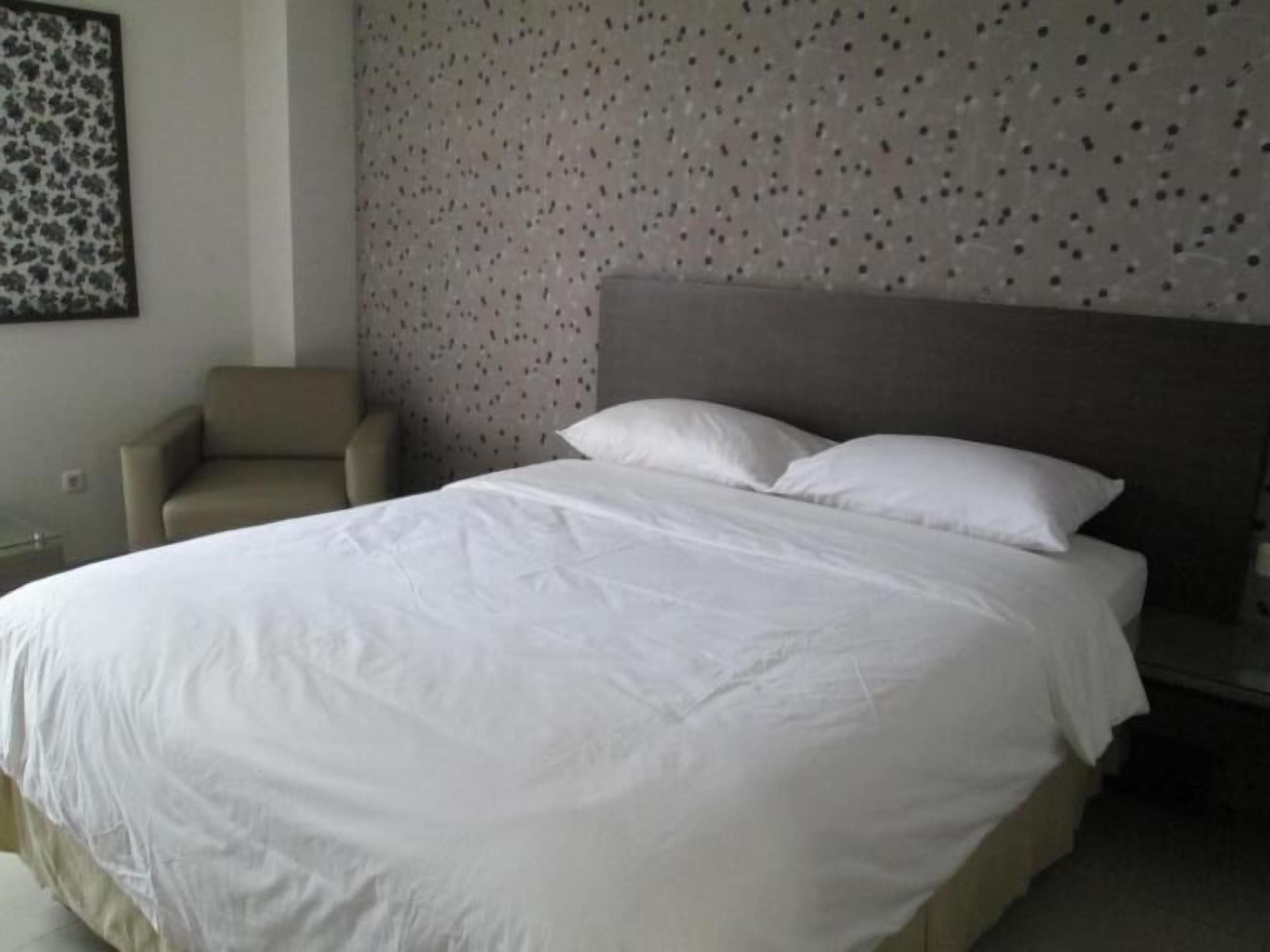A neatly made bed with white linens in a hotel room.