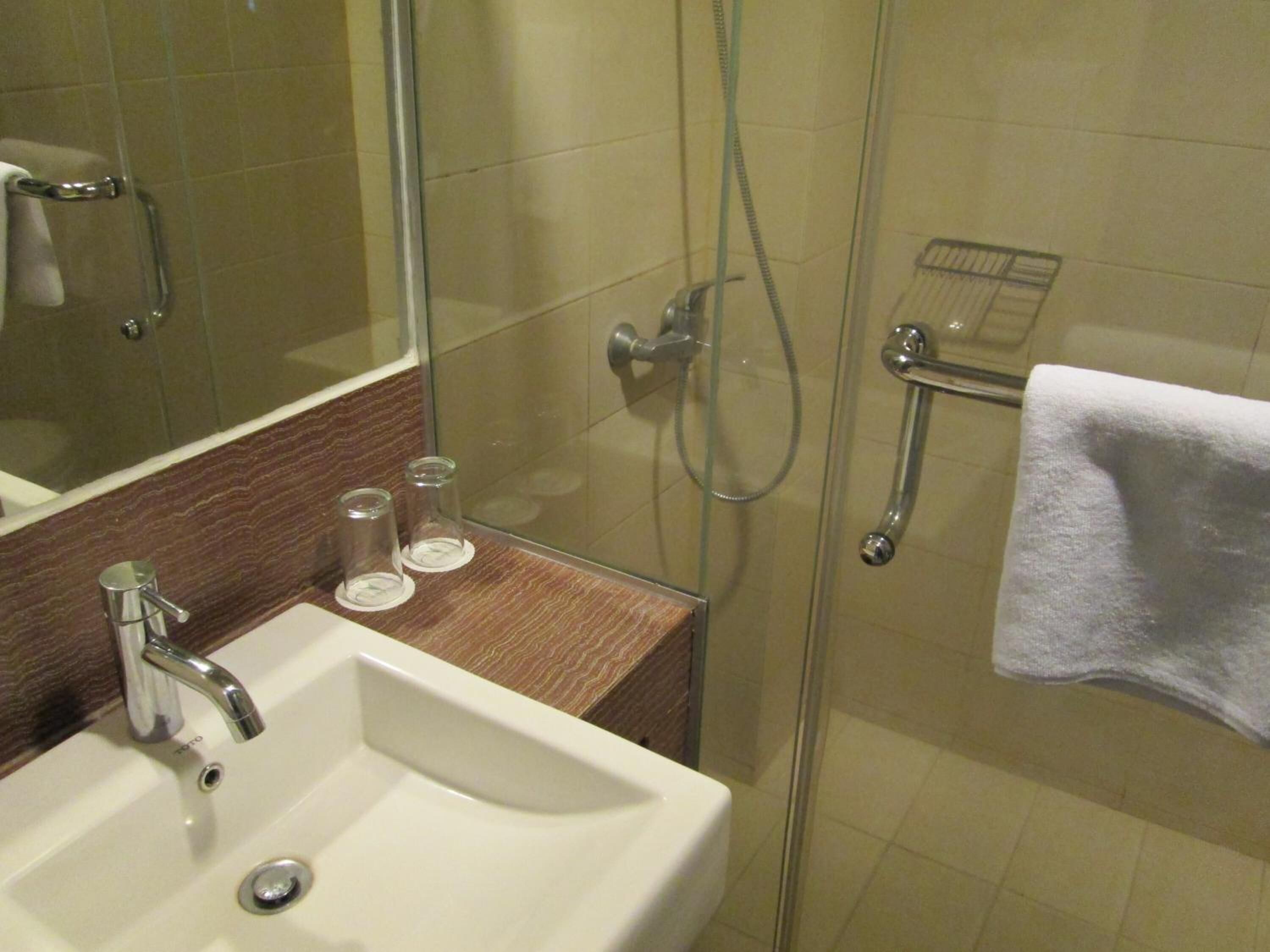 Un baño con cabina de ducha de vidrio, un lavamanos con espejo y un perchero para toallas.
