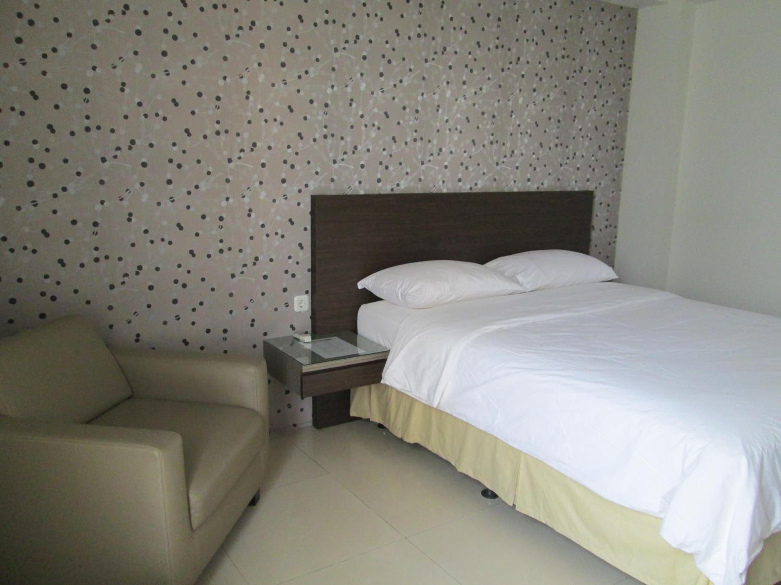 A hotel room with a bed, a nightstand, a chair, and a polka dot wallpaper.