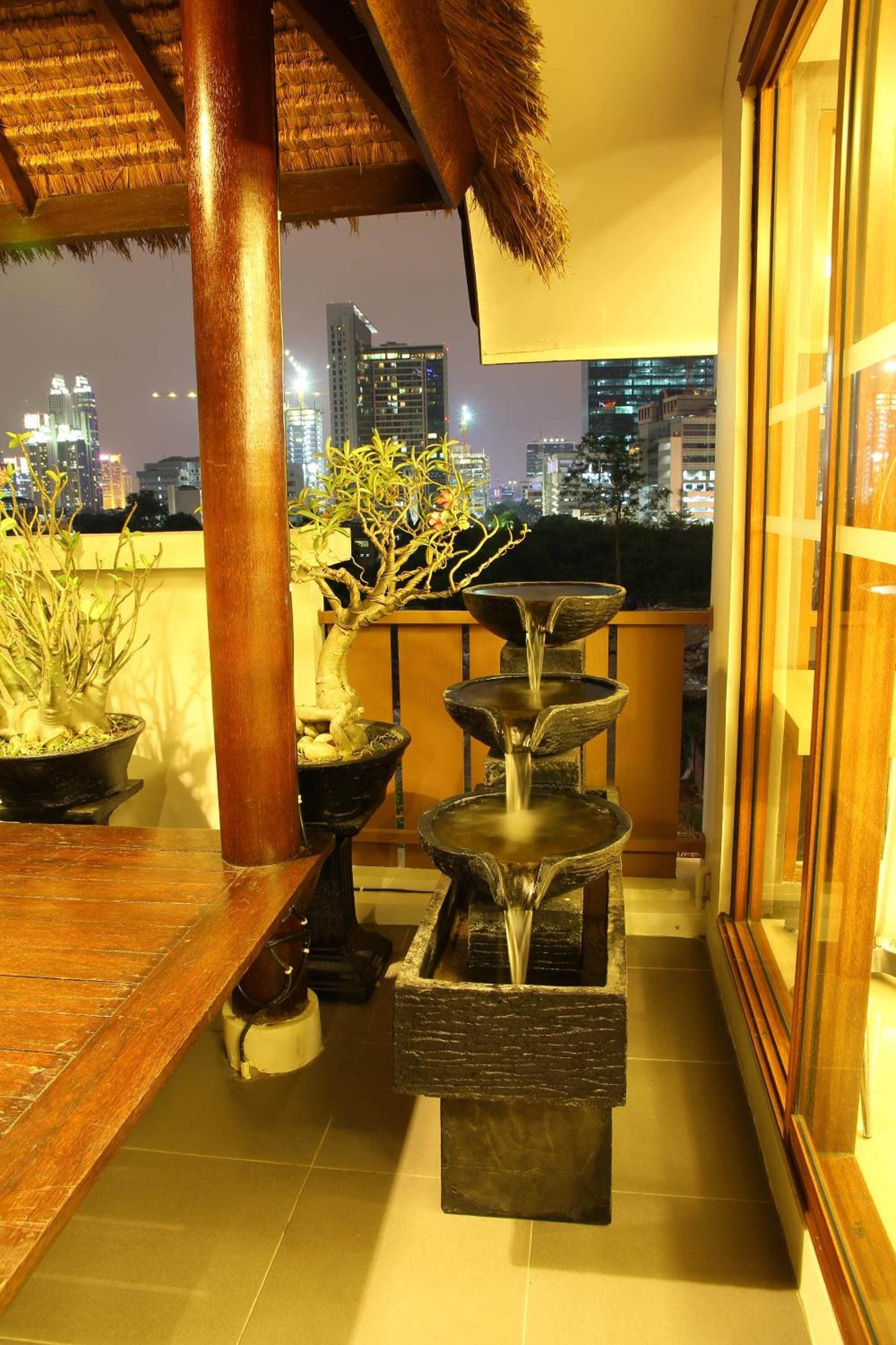 A balcony with potted plants, a wooden table, and a tiered water feature.