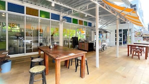 An indoor café with wooden tables and stools, large windows, and a metal roof. - Sabai Inn (Pattaya)