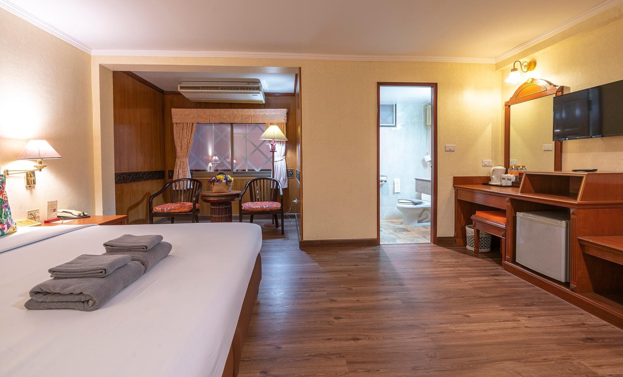 Habitación de hotel con cama, escritorio con lámpara, televisor y baño visible a través de una puerta abierta.