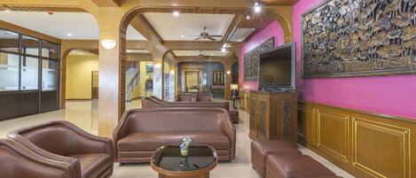 A spacious living area with leather sofas, a coffee table, and a flat-screen TV mounted on a wall with a floral mural.