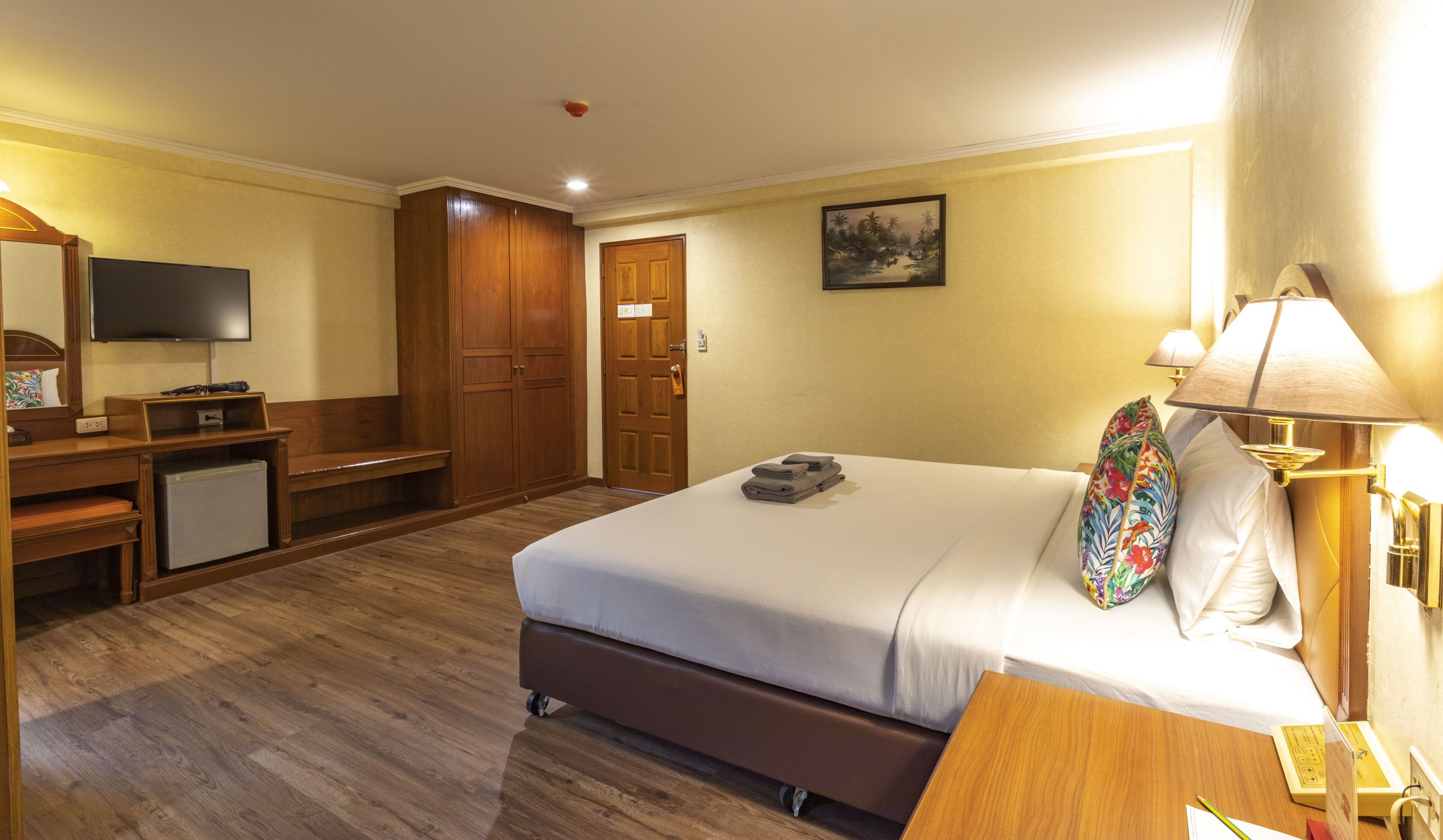 Habitación de hotel con cama, escritorio con televisor, armario y un cuadro en la pared.