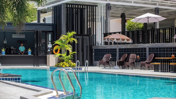 A swimming pool with lounge chairs and umbrellas, surrounded by a building with a covered patio area. - Sabai Inn (Pattaya)