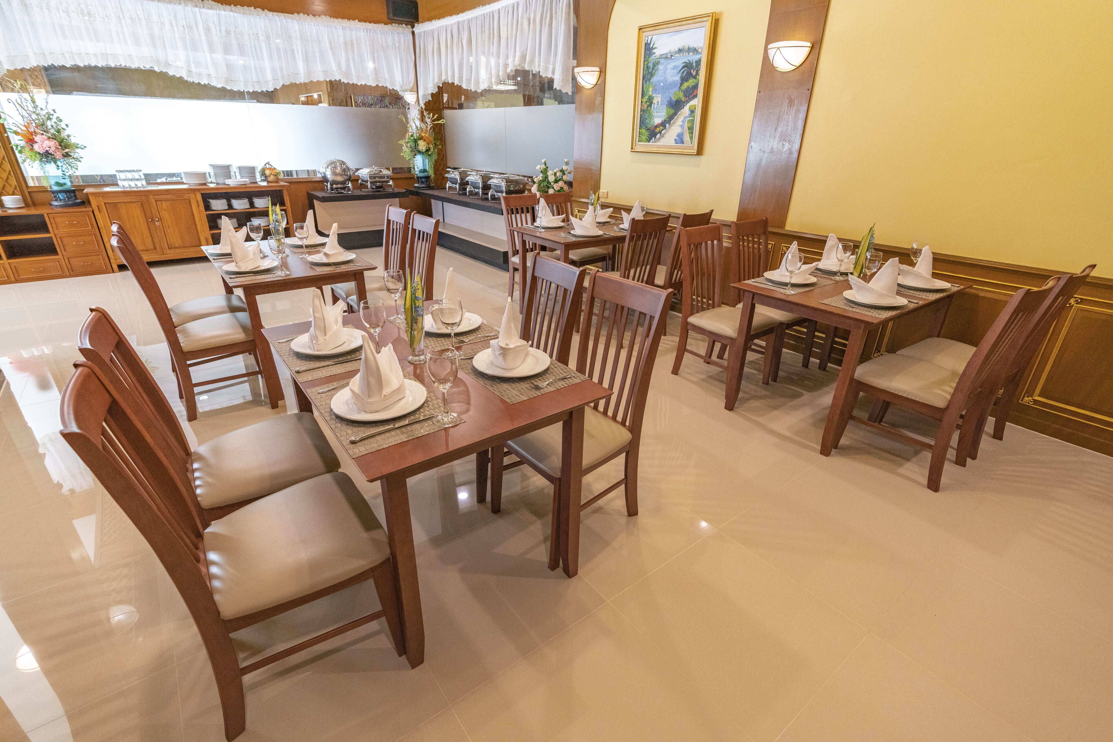 A dining area with wooden tables and chairs, neatly set with white tableware and glassware.