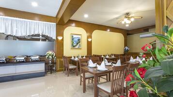 Un comedor con mesas y sillas de madera, una barra de buffet y un ventilador de techo.