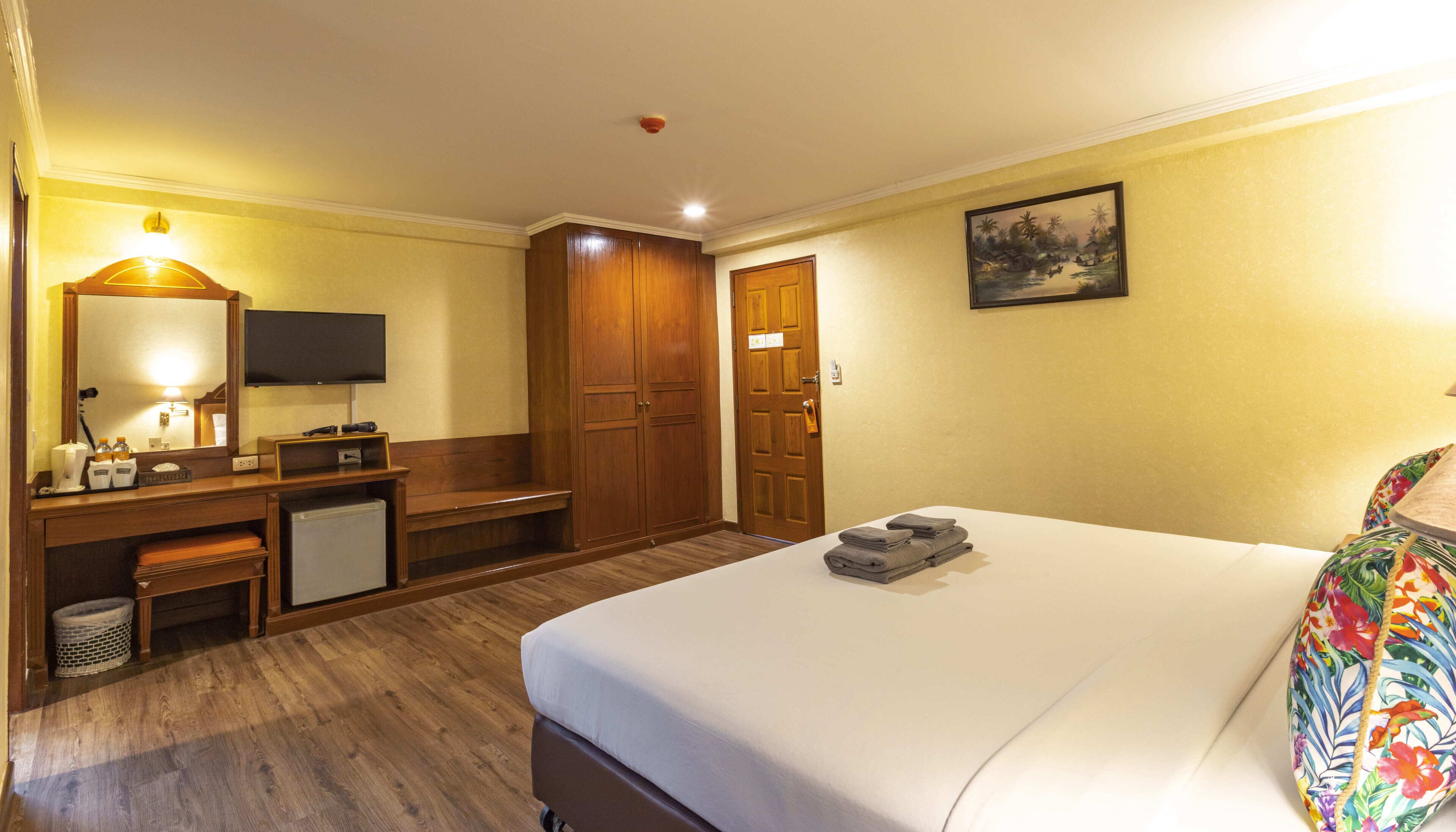 A hotel room with a bed, a desk with a computer, a television, and a wooden wardrobe.