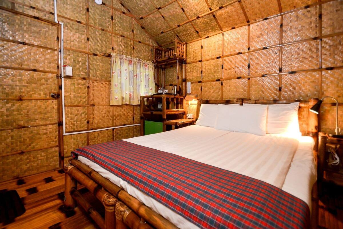 Una habitación con una cama, cabecera de madera, mesita de noche, lámpara y un muro con diseño tejido.