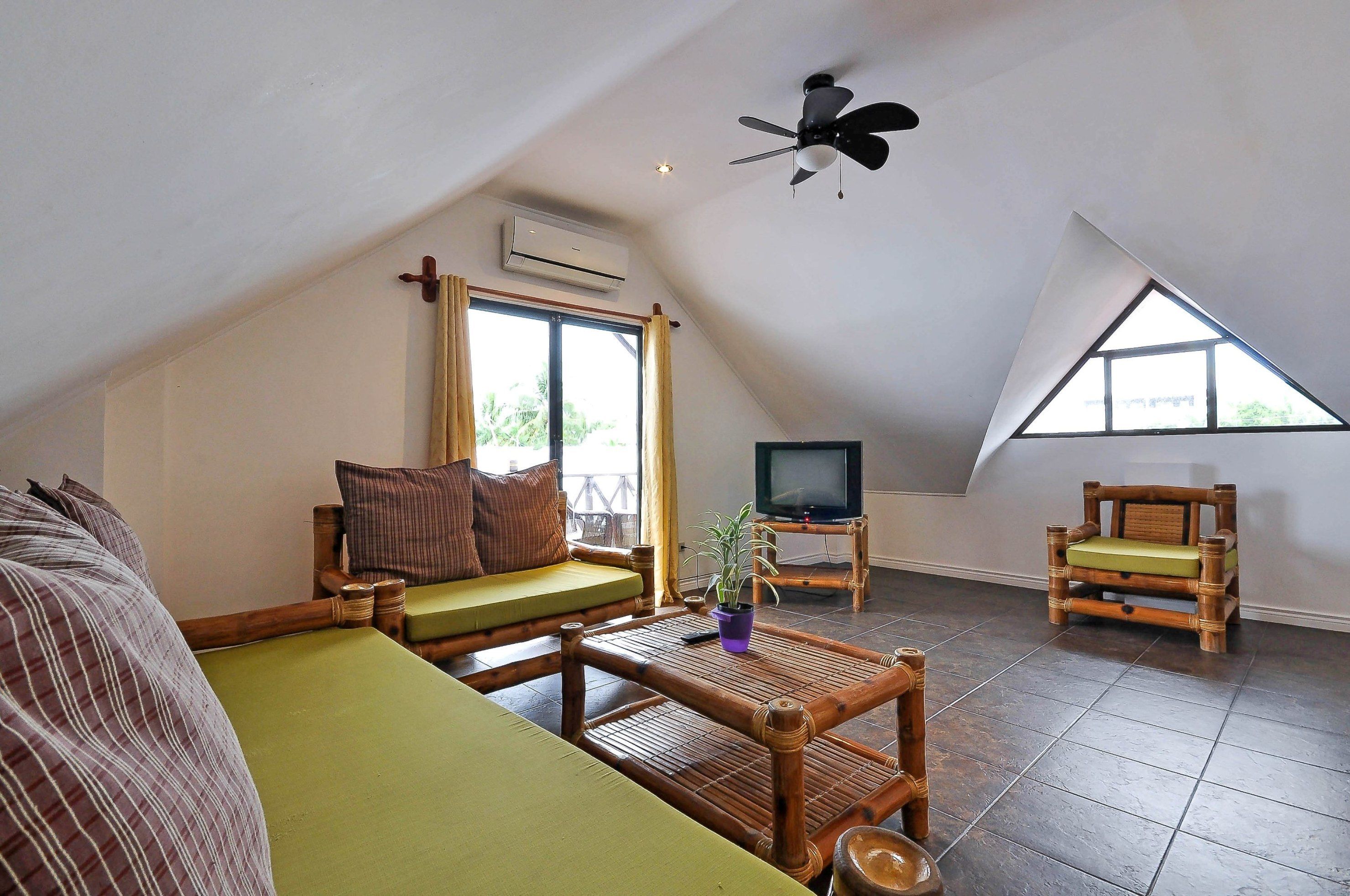 Una habitación acogedora estilo loft con techo alto, ventilador de techo, televisor, una peque ña mesa de madera y una zona de estar con sofá y sillón.