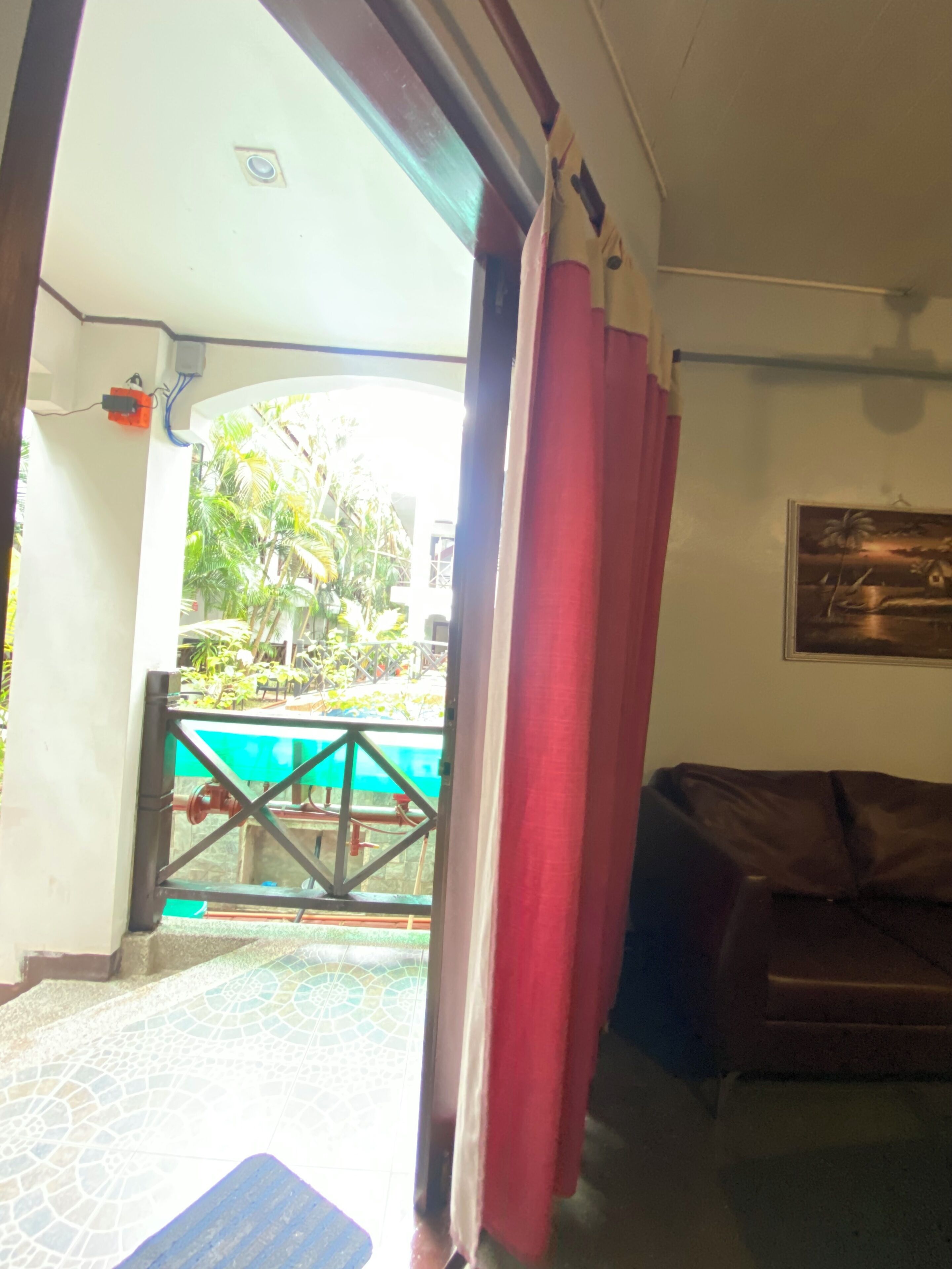 Un espacio interior con vistas a una zona de piscina exterior, un sofá de cuero marrón y un cuadro en la pared.