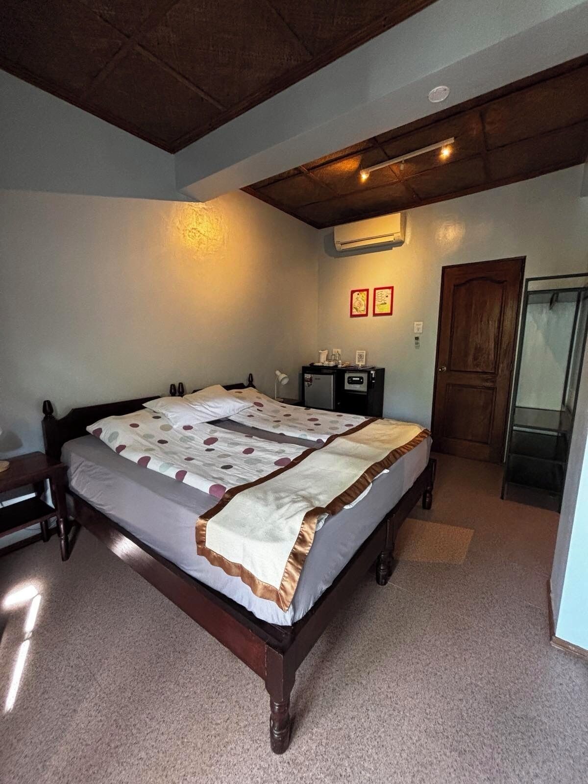 Une chambre à coucher avec un lit en bois, une table de chevet, un bureau, une chaise, une armoire et une porte.