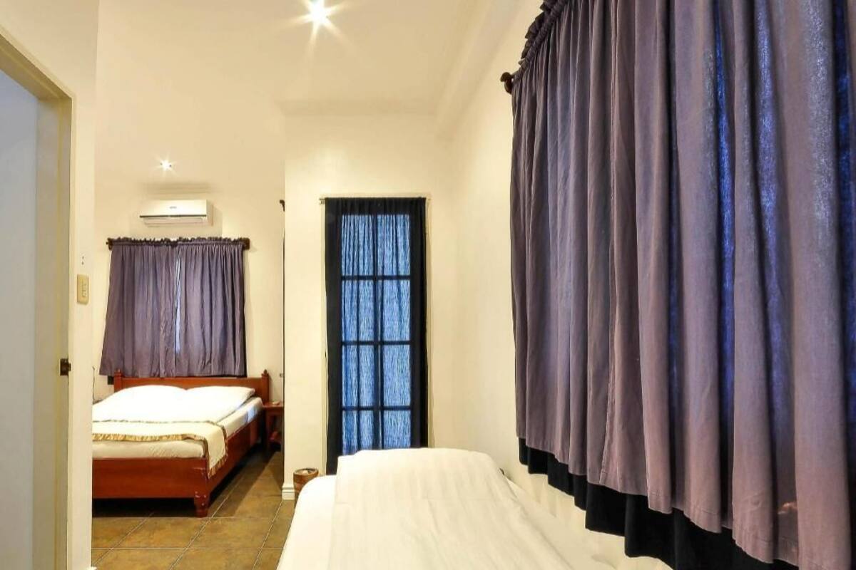 Una habitación de hotel con cama, ventana con cortinas, mesita de noche y equipo de aire acondicionado.