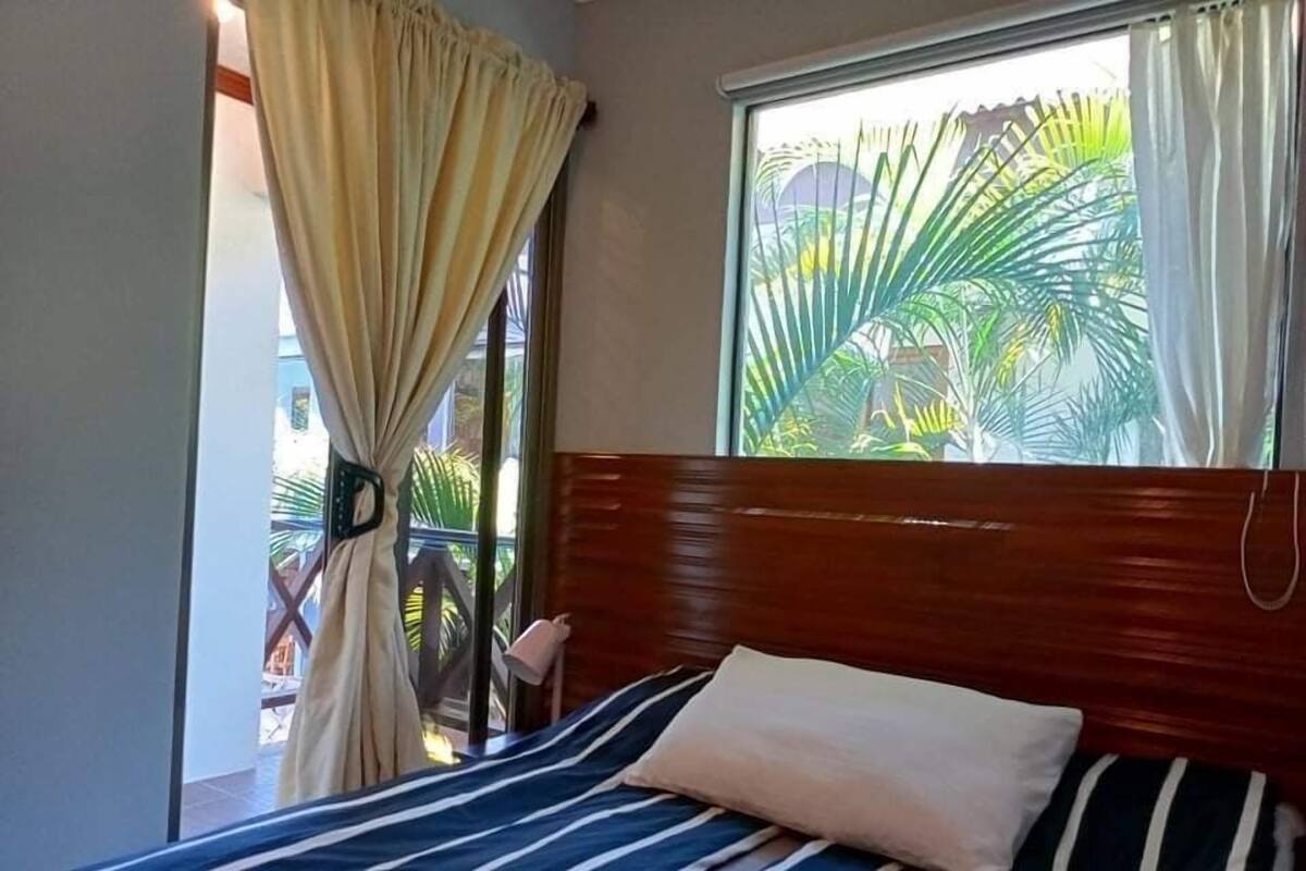 Una cama con una colcha a rayas, una almohada, un cabecero de madera y una ventana con cortinas.