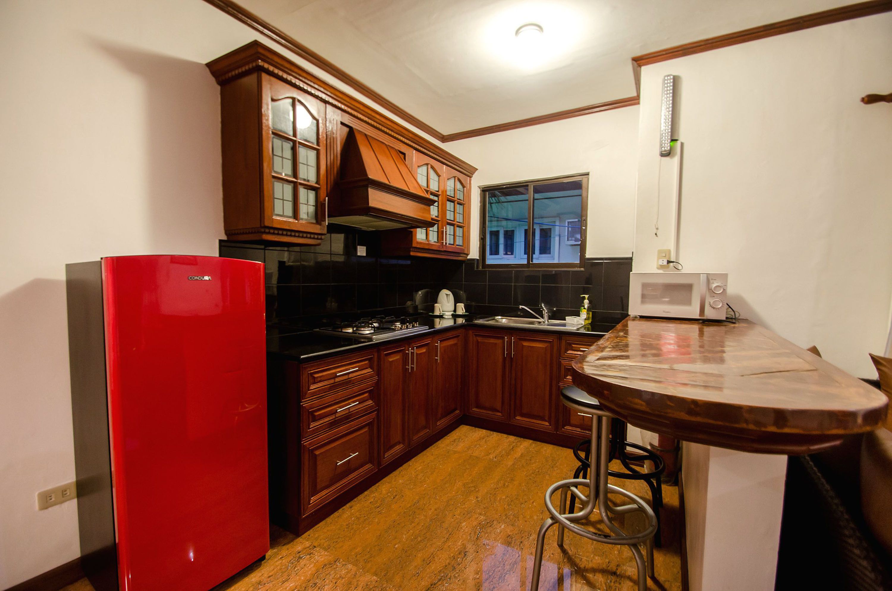 Una cucina con mobili in legno, un frigorifero rosso, un forno a microonde e una finestra.