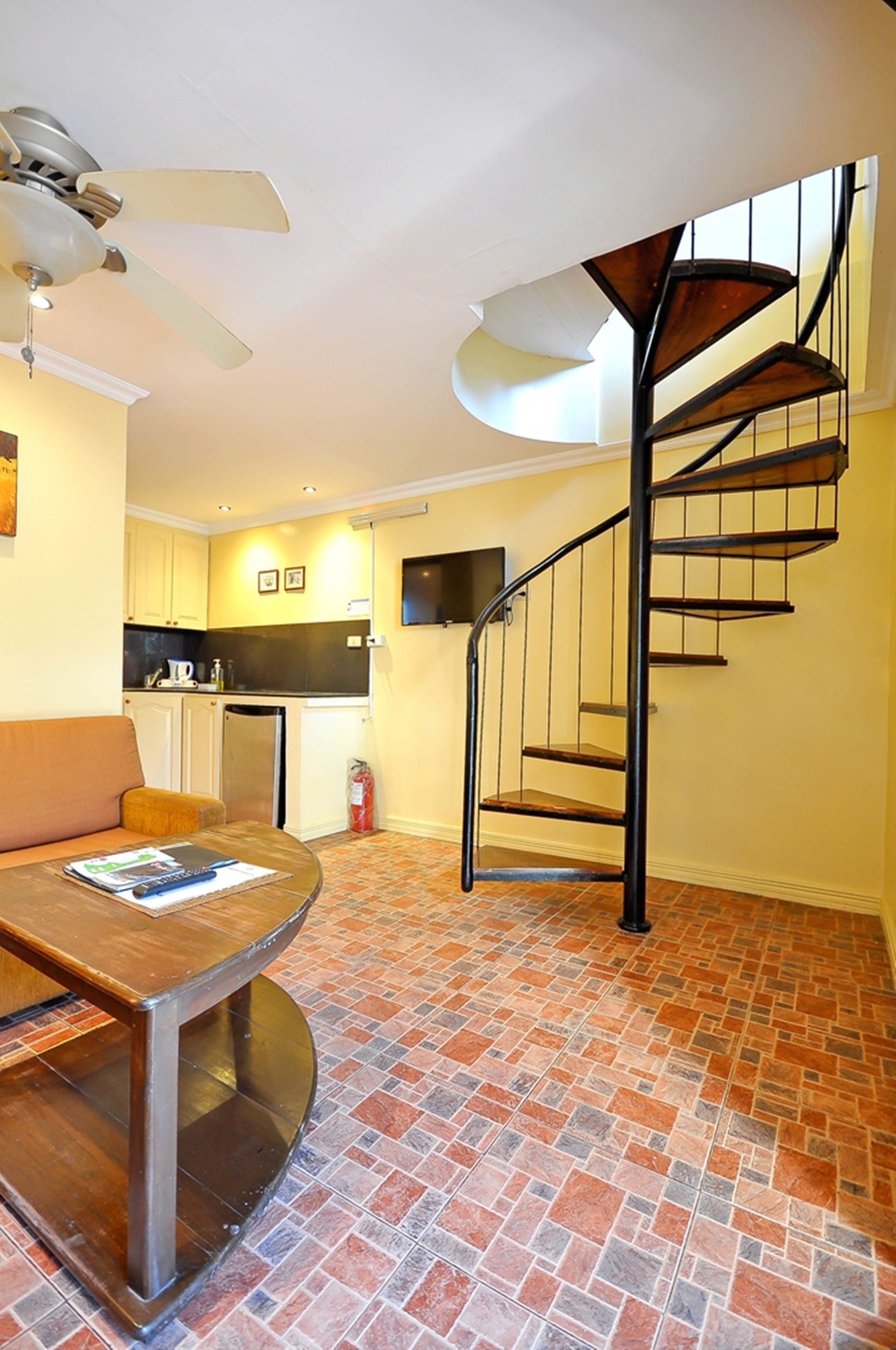 Un intérieur moderne avec un escalier en colimaçon, un coin repas avec une table et des chaises, et une cuisine en arrière-plan.
