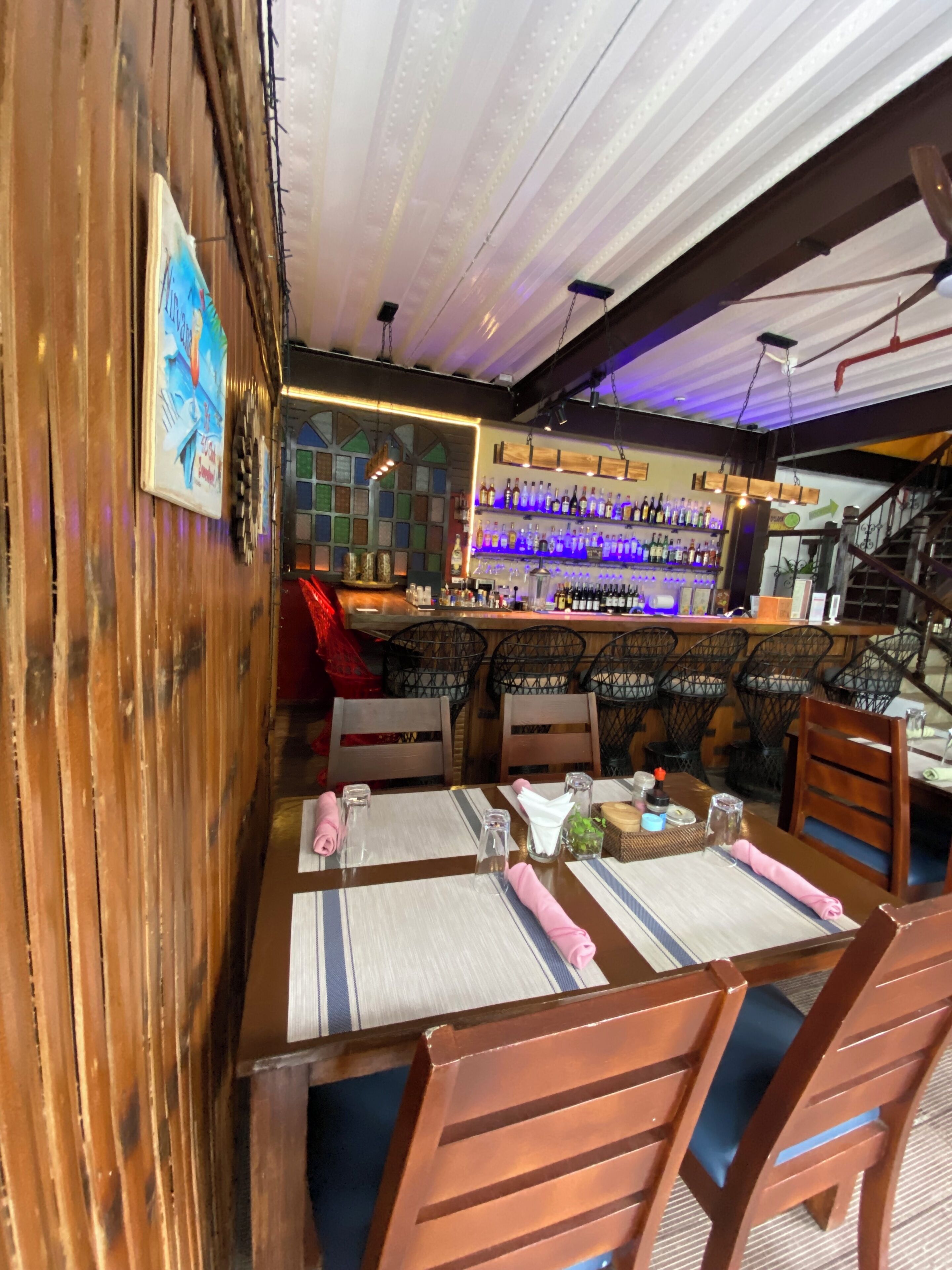 A restaurant with wooden walls, a bar area with shelves of bottles, and tables set for dining.