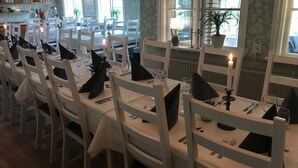 Un espace repas avec des tables et des chaises blanches, des bougies et des plantes en pot.