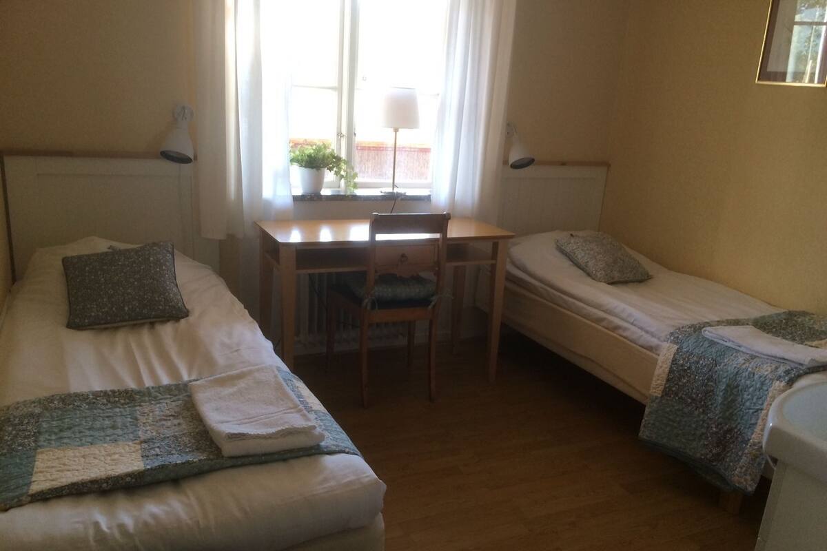 A room with two single beds, a desk with a chair, and a window with curtains.