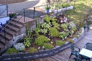 A garden area with a stone retaining wall, steps leading up to a deck, and outdoor seating. - Hotell Paradis (Eksjo)