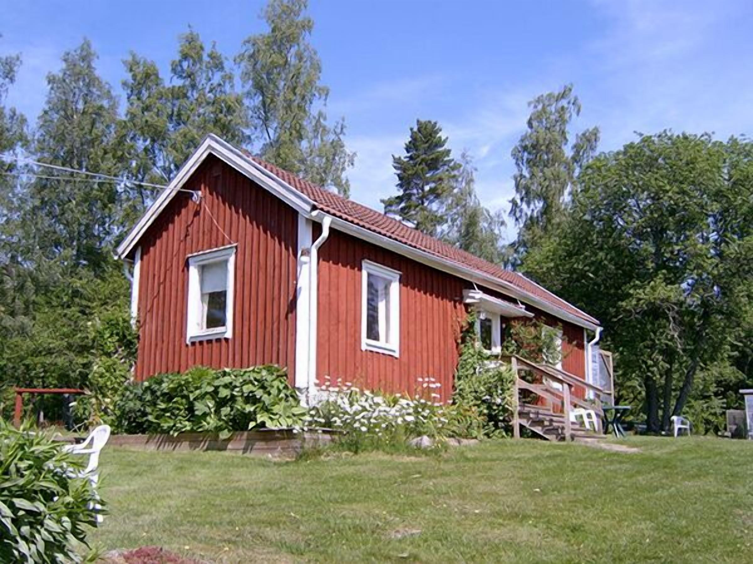 A red wooden house with a gabled roof, surrounded by a grassy yard and trees.