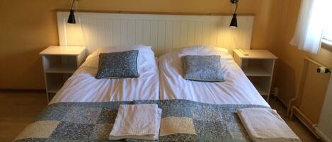 A double bed with two pillows, a quilt, and two bedside tables with lamps.