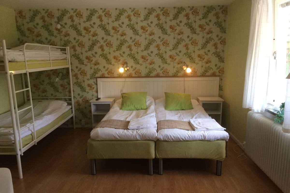 A dormitory room with bunk beds, two bedside tables, green pillows, and a radiator.